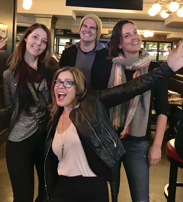 Four people posing and smiling for the camera. They look excited and happy.